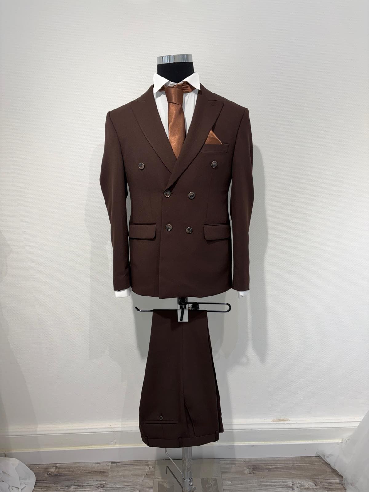 Vue du haut d'un costume de mariage croisé marron sur mannequin, chemise blanche et accessoires.