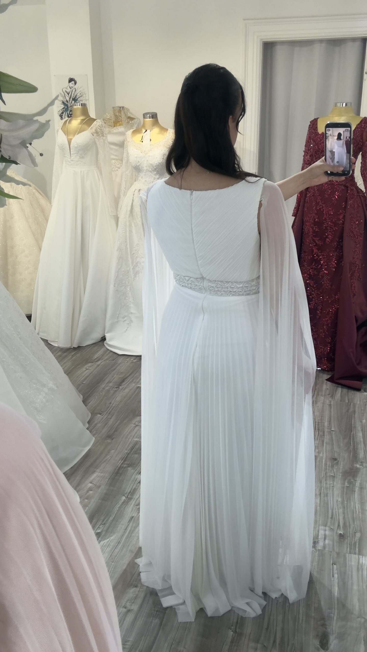 Vue du dos d'une robe de soirée blanche plissée avec ceinture ornementée.