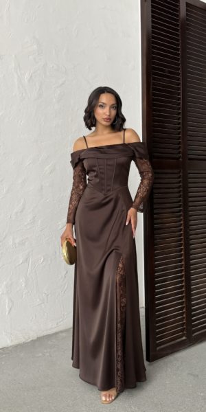 Vue en pied d'une femme portant une longue robe de soirée marron chocolat en satin avec épaules dénudées, manches en dentelle transparente et fente haute révélant des détails en dentelle.