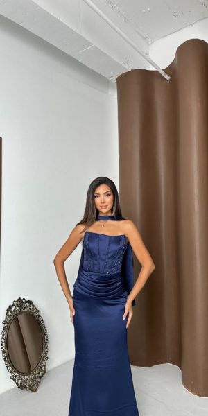 Mannequin de face portant une robe de soirée longue bleu marine en satin avec un corset structuré, des détails perlés sur le bustier et un foulard assorti pour Keya Mariage.